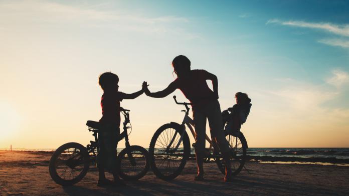 happy mother with kids biking at sunset
