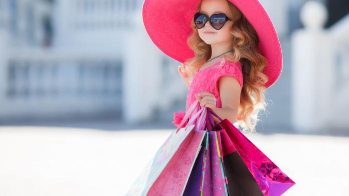 Cute little girl in fashion hat with shopping bags next to a supermarket