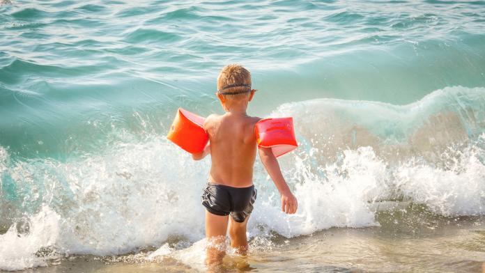 child runs in the sea with protective inflatable sleeves