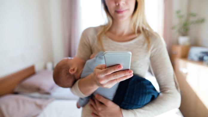Mother with baby son in her arms and smartphone, texting