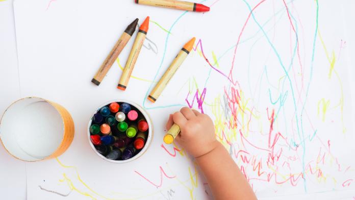 Baby's hand drawing on the white paper with colorful crayons