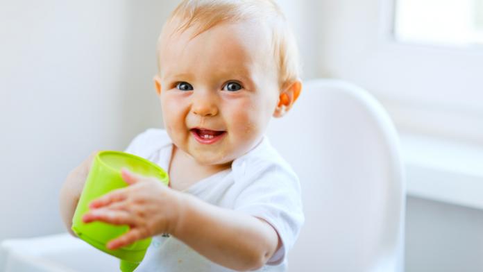 Cheerful baby girl sitting in chair and holding cup