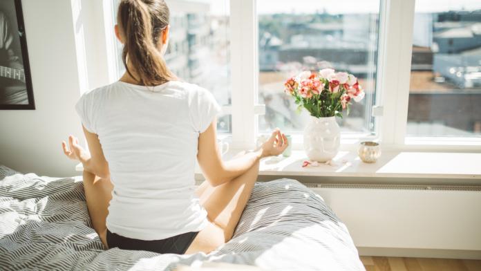 Beautiful woman practicing yoga in front of window of cozy apartment.Relaxation and mindfulness concept.