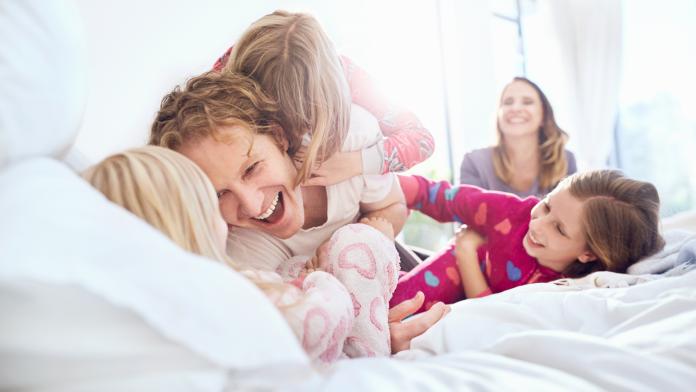 Playful father and daughters tickling on bed