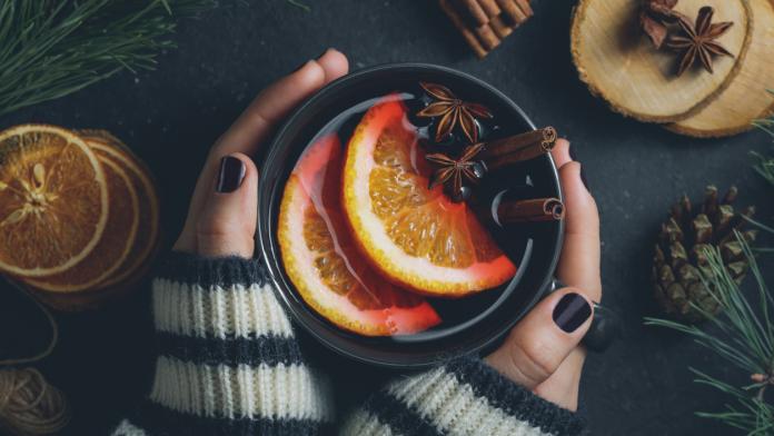 Top view of the girl's hands in a winter sweater are holding a big black cup with hot mulled wine. The concept of cozy winter Holidays.