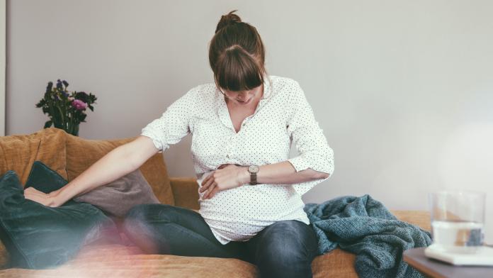 Expectant mother timing her contractions while sitting on couch at home