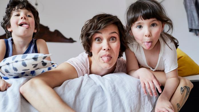 Portrait of mother, son and daughter, lying on bed, poking tongue out alleenstaande mama
