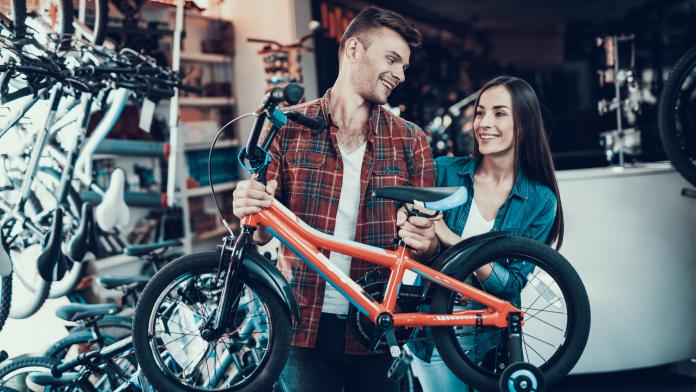 Happy Young Couple Chooses Kids Bicycle in Store kinderfiets kopen