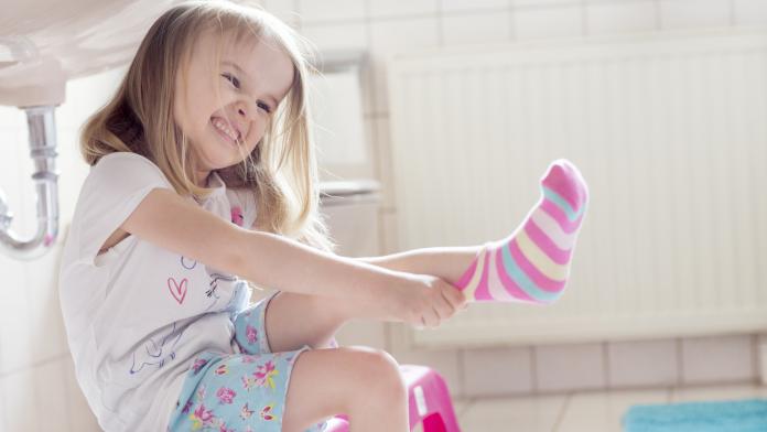 Child (4-5) pulling socks on with determined facial expression zweetvoeten kind