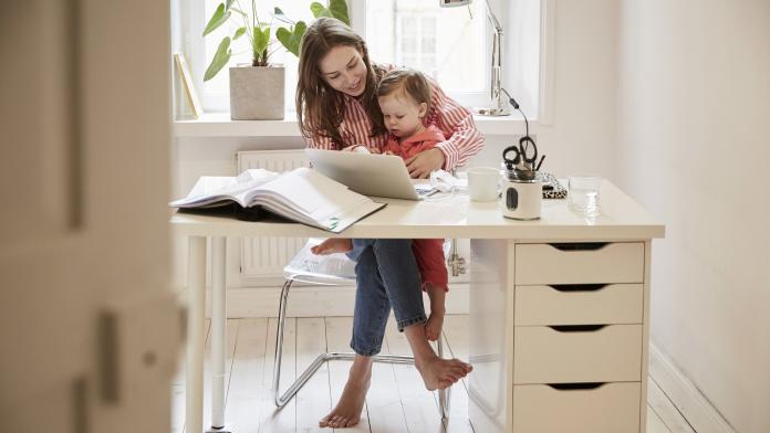 Female accountant sitting with daughter while working on laptop at home