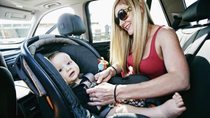 Mother buckling baby son in car seat