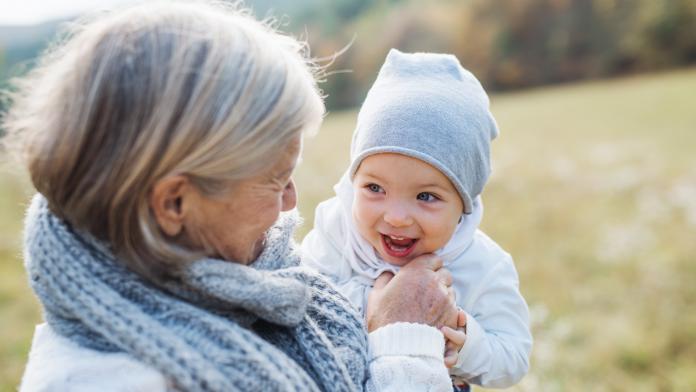 A portrait of senior grandmother outdoors holding a toddler granddaughter in nature. oma baby