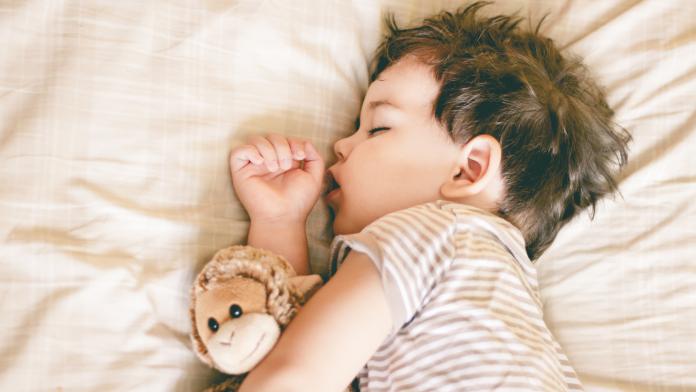 Boy sleeping on bed holding a soft toy by his side