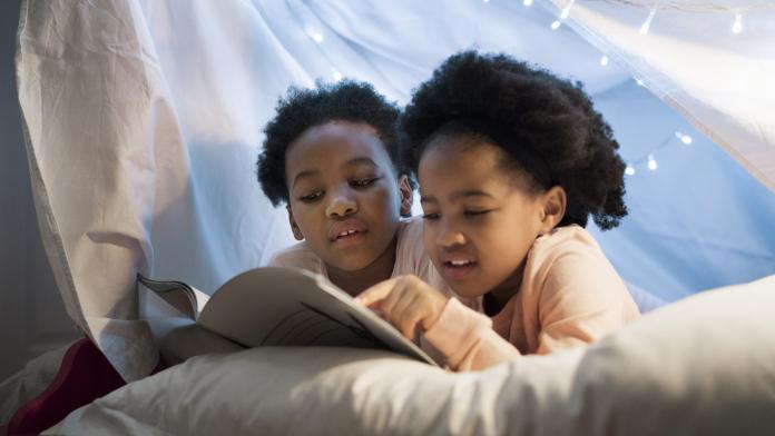 Girls reading story book while lying on bed kinderen samen op een kamer
