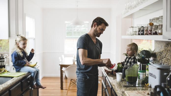 Mid adult man with daughters cooking food in kitchen at home dagroutine voor je kinderen