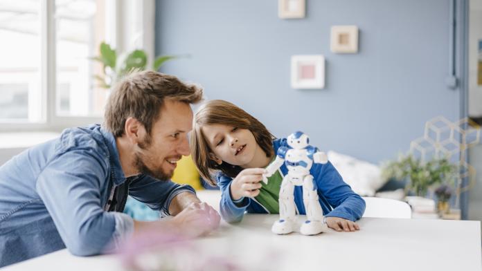 Happy father and son playing with robot on table at home connected toys