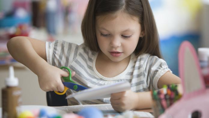 Caucasian girl cutting paper with scissors knutsel peppa pig