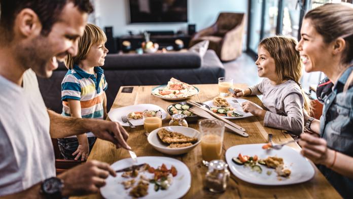 Young happy family talking while having lunch at dining table. Opvoeden na corona