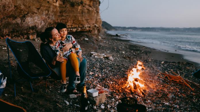 Mother and child enjoying campfire on beach at sunset gadgets kamperen