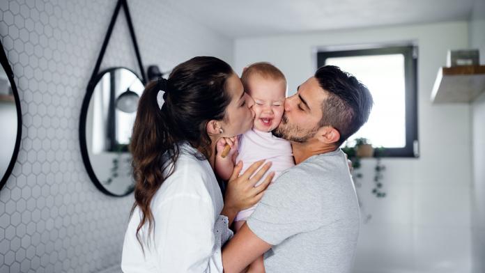 Portrait of young couple with toddler girl in the morning indoors in bathroom at home, kissing. Klaar voor kinderen?