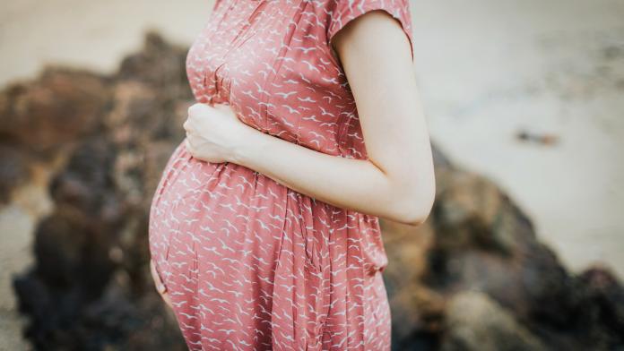 Close up of an expecting pregnant woman wearing a pink dress and holding her belly and relaxing outdoor