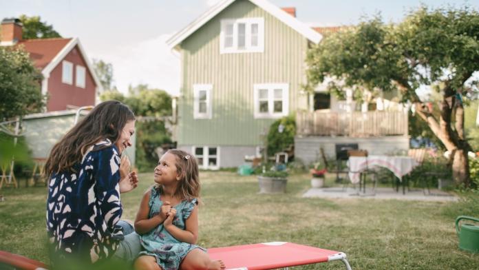Smiling mother and daughter talking while sitting on lounge chair in backyard