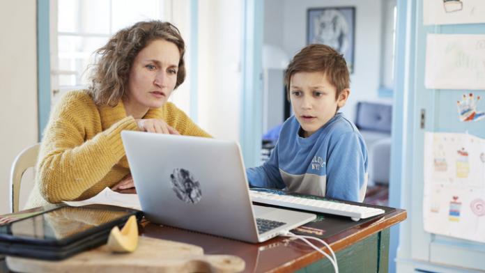 Mother homeschooling son at laptop lezen en schrijven