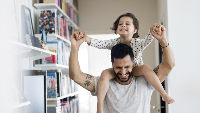 Happy father carrying girl on shoulder while standing at home