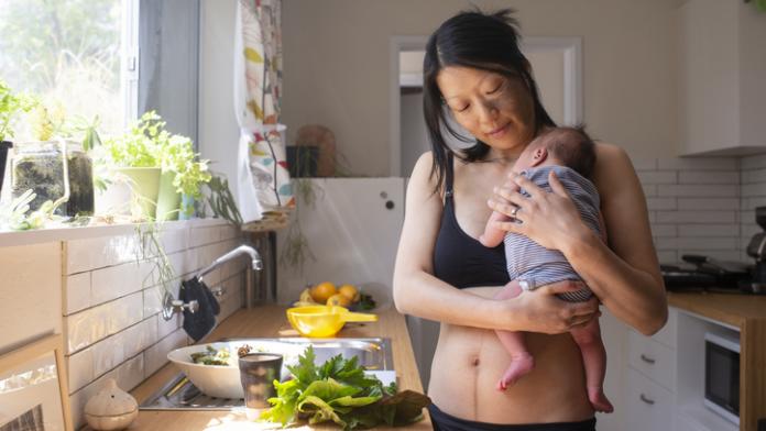 one woman with a young baby making a salad in the kitchen