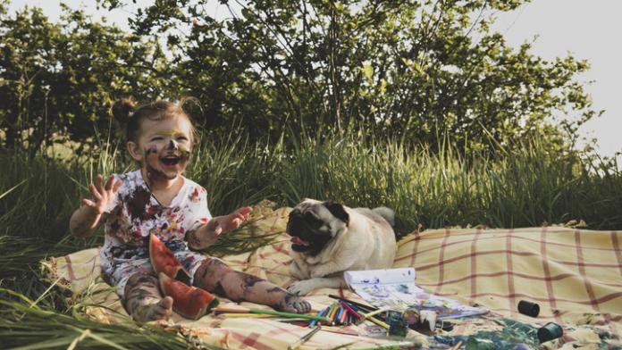 A little girl stained in paint is playing with her dog in the forest. eetbare verf