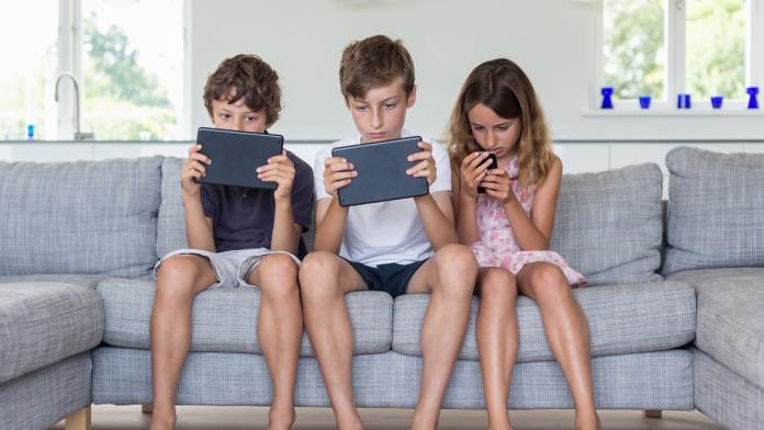 Brothers and sister on sofa with digital tablets and mobile