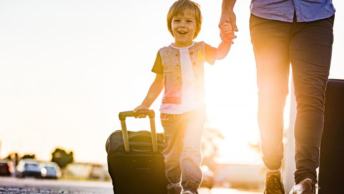 Happy boy having fun while pulling suitcase with his parent at sunset.
