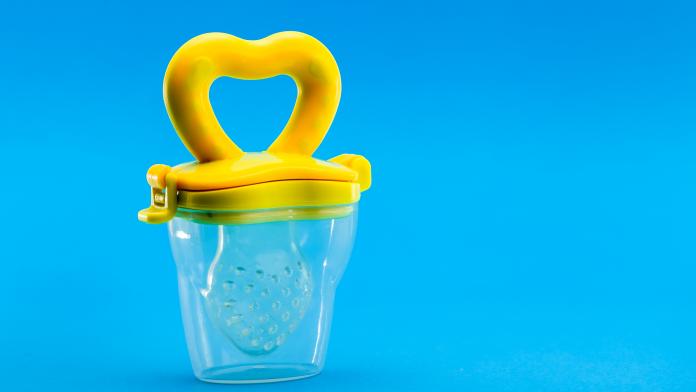 Fruit feeder in a plastic case with a yellow handle and a silicone pacifier on a blue background with a copy space.