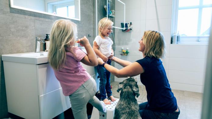 Smiling mother bonding while kneeling in bathroom by dog at home