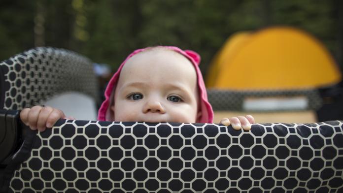 Baby standing in travel crib at campsite. reisbedje kopen