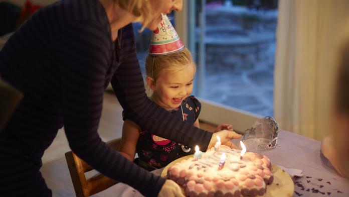 Mother sets birthday cake in front of smiling little girl vier jaar verjaardag cadeau