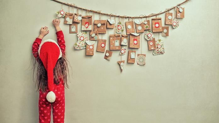 child in pajamas and Christmas cap stretches for advent calendar with small gifts. kid counts days until new year advent diy kerst