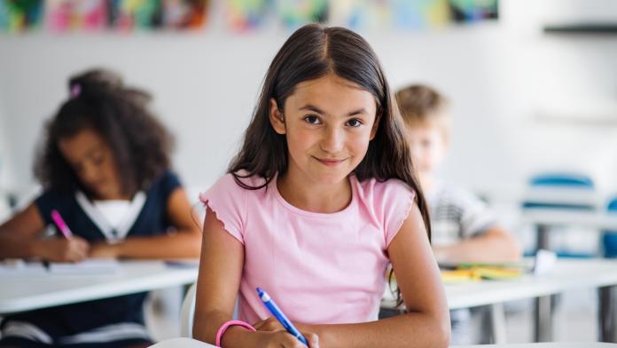 A small school girl sitting at the desk in classroom, looking at camera. pleaser grenzen aangeven weerbaar