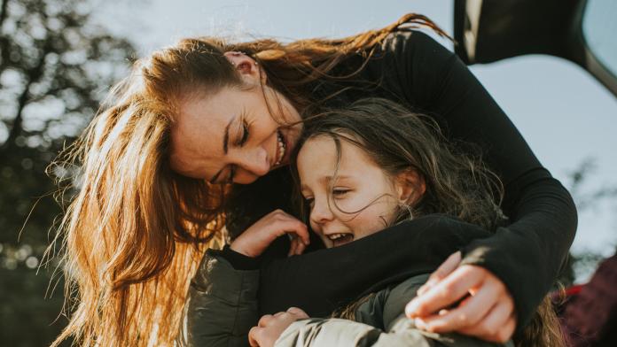 A mother bends down to embrace her daughter from behind pleegzorg
