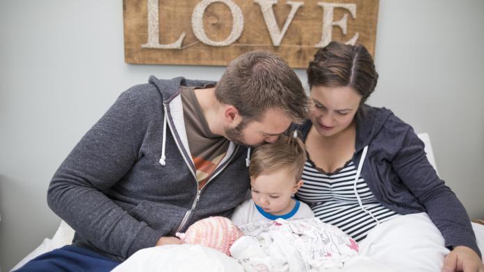 Loving parents with son and newborn daughter sitting on bed at home geboortehuis birth and breakfast vroedvrouw