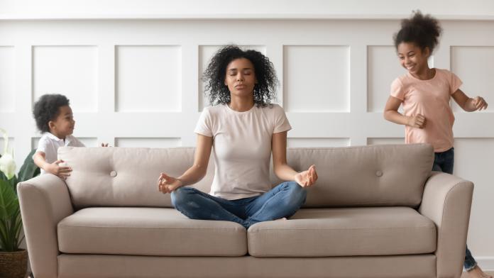 While noisy kids running young african mother meditates on couch geduld bewaren schreeuwen opvoeding