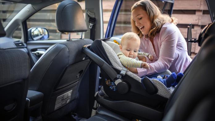 Mother putting her son in a car safety seat