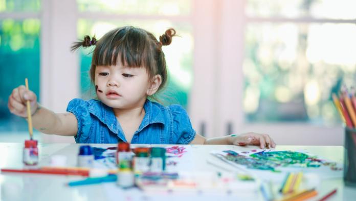 little girl painting with paintbrush and colorful paints on desk background Zomerse knutselideeën