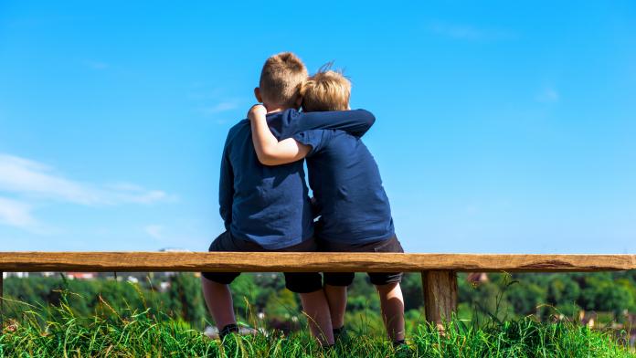 Two friends hug each other while sitting on a bench outside empathie inleven gevoelens emotie