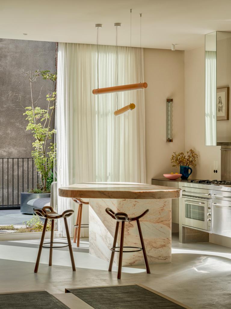 Boven het kookeiland in Rose Aurore marmer hangen twee Aura Lights van Sabine Marcelis voor Established & Sons. Vintage krukken van Carl Malmsten. Let op de dampkap boven het fornuis: dankzij de spiegels gaat die op in de ruimte.