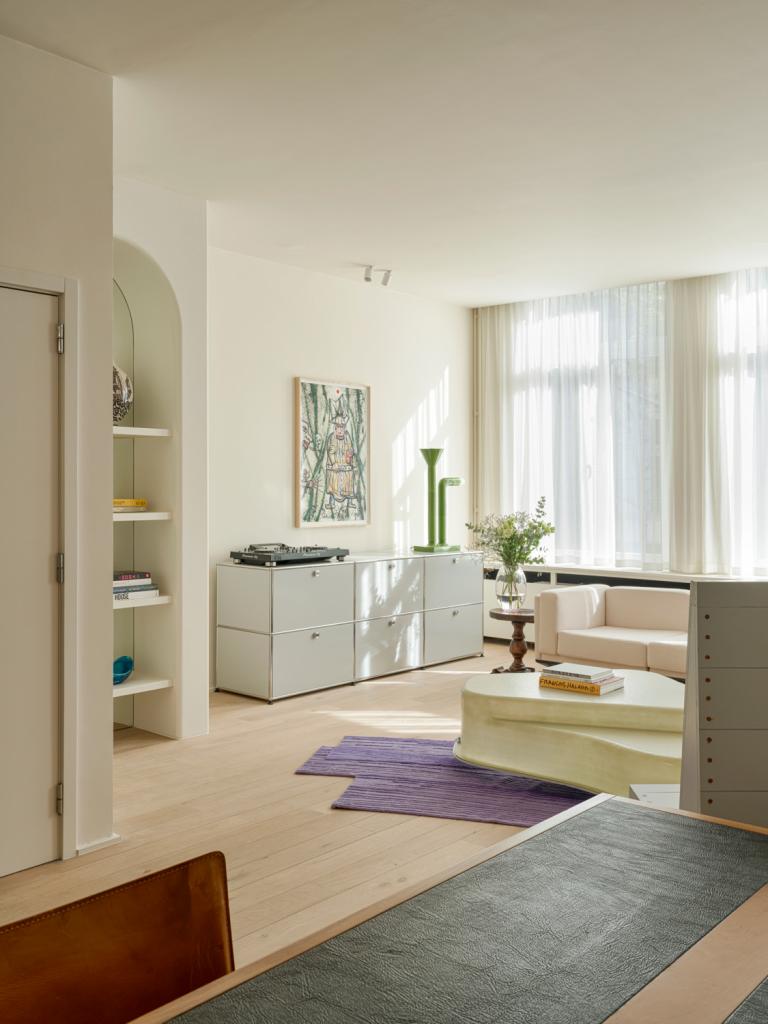 In de woonkamer is de sofa Italiaans design uit de jaren ’70.  Boven het dressoir van USM Haller hangt een werk van Fred Bervoets die Sarah van haar grootvader erfde. De groene lamp is van Adelie Ducasse, gekocht bij Galerie Scene Ouverte