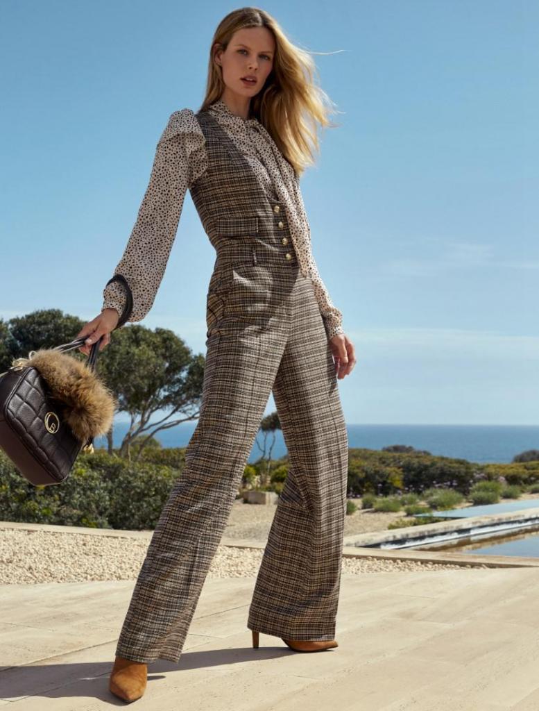 Mix van stoer en vrouwelijk: geruite jumpsuit (220 euro), romantische bloes met strik (175 euro), cognackleurige laarsjes met hoge hak (285 euro) en handtas (165 euro), van Caroline Biss.