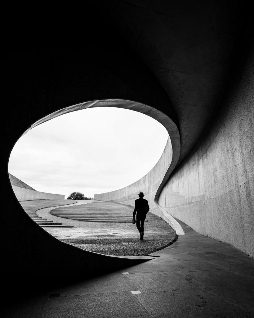 Sofie Steenhoudt (56) - Sint-Eloois-Winkel: “De kleine mens omringd door prachtige architectuur”Naast haar job als administratief bediende is Sofie Steenhoudt fotografe in bijberoep. Sofie is altijd op zoek naar intrigerende locaties. Frisse en hedendaagse zwart-wit fotografie is helemaal haar ding. “Deze foto is een goede representatie van alles wat ik graag zie in mijn werk: de compositie, de vormen, het contrast en het licht. Een persoon omringd door de geometrische vormen van prachtige, minimalistische architectuur, met oog voor detail. Het toont aan hoe klein we soms zijn in de grote wereld.”