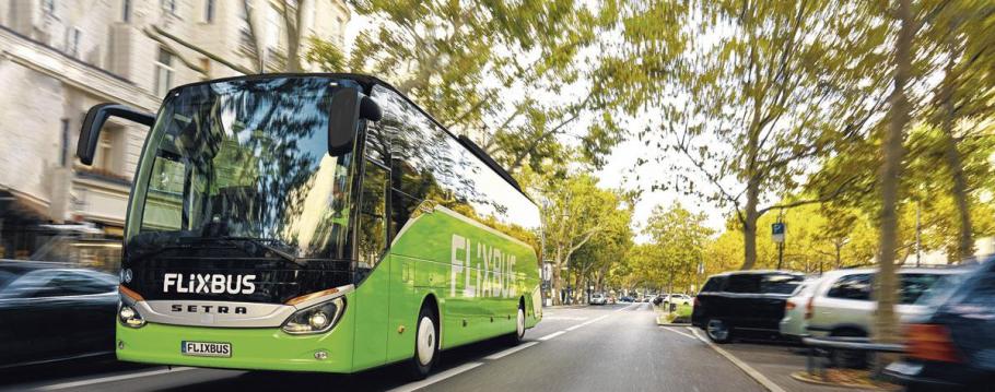 Un des bus verts de FlixBus roulant dans une rue arborée