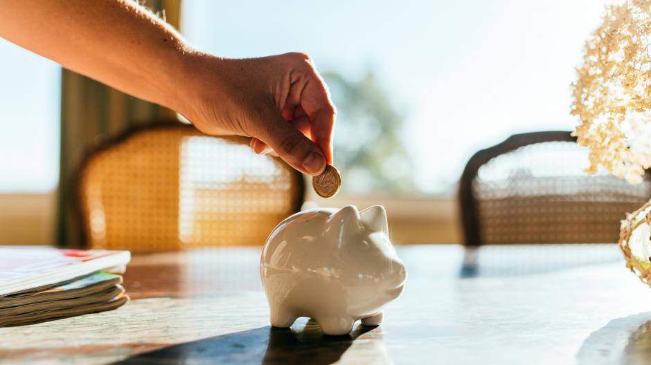 Een vrouw die een euromuntstuk in een spaarvarken steekt. (on)verwachte kosten opvangen doe je met deze tips.